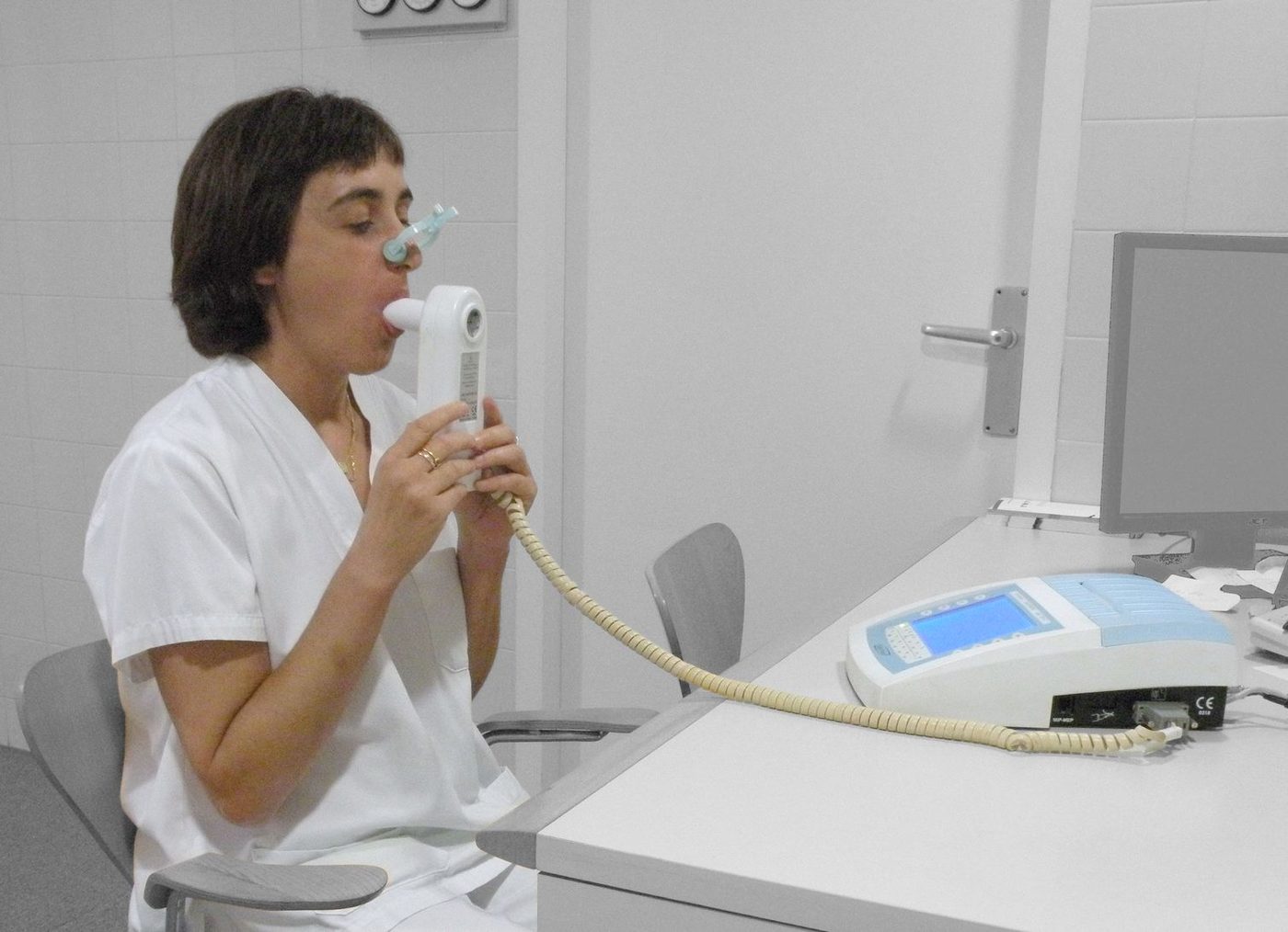 Person using a spirometer with a mouthpiece and nose clip to measure breathing.